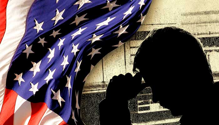 United States flag with figure of a man in shadow holding his head in his hand.